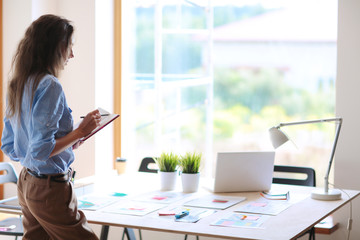 Young woman standing near desk with instruments, plan and laptop