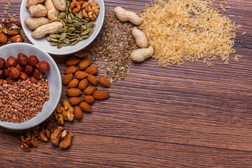 Assorted nuts in white bowl, plate on wooden surface. Top view with copy space