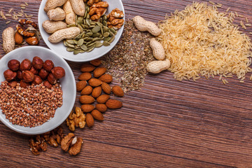 Assorted nuts in white bowl, plate on wooden surface. Top view with copy space