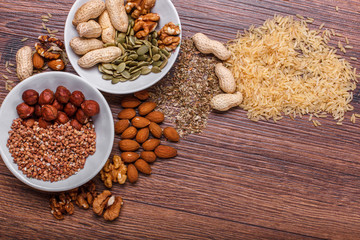 Assorted nuts in white bowl, plate on wooden surface. Top view with copy space