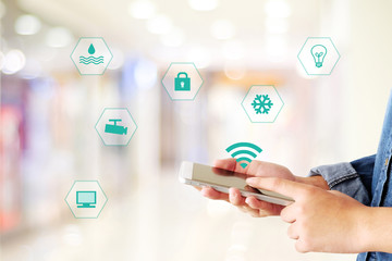 Hand using smart phone as smart home control application over blurred bokeh background, smart home concept