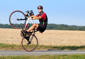 Cheerful cyclist riding on the rear wheel. Biker balancing while driving on a road bike. Risky ride on one wheel.