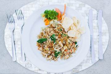 Traditional indonesian nasi goreng with chips, fresh tomato and greens on white plate and silver cutlery on tray