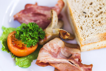 American breakfast with fried sausages, tomato, bacon, toasts and greens close up. Fat and unhealthy food