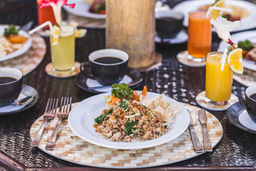 Traditional indonesian breakfast nasi goreng with bali kopi on white plate and silver cutlery on tray.  Table with different meals and fresh juices