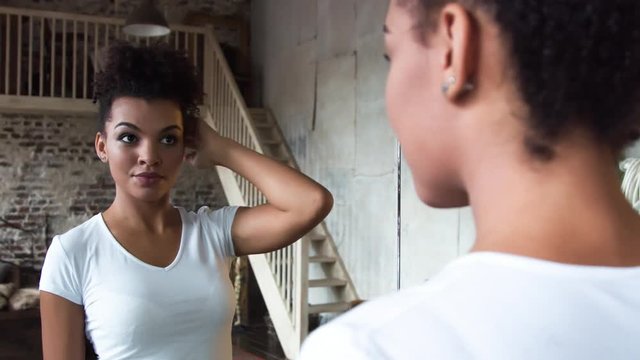 Attractive african-american girl corrects hair standing in front of a mirror.