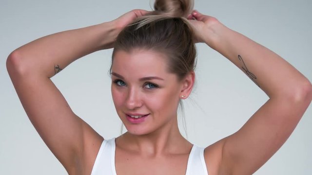 Attractive blonde woman straightens hair on white background.