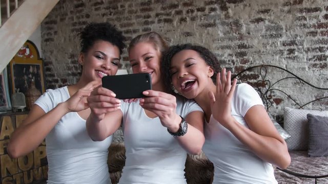 Beautiful and funny girls in white T-shirts makes selfie. Two afro-americans and one european girls.