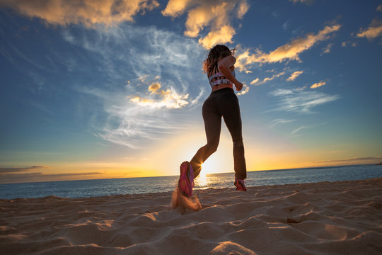 Running girl jogging at beachside at sunset time. Motion blurred image
