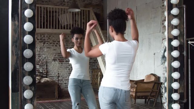 Attractive african-american girl corrects hair standing in front of a mirror.