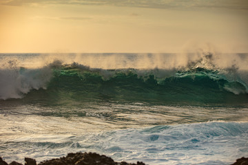 Beautiful ocean wave crashing against rocky coast at sunset time. Sea scenery with splashing water and white foam marine background