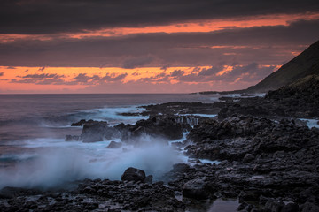 Obraz premium Beautiful sunset in ocean view with pinky orange sky on background. Rocky coastline with splashing against black lava rocks waves