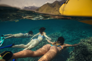 Girls swimming underwater by a yellow boat on water surface. Mountains on background. Water line...