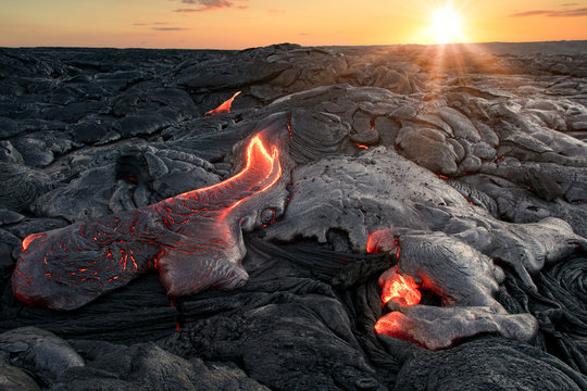 Black lava field with hot red orange Lavaflow at sunset background