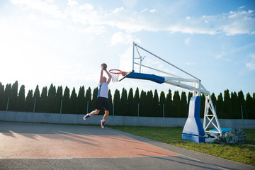 Young man jumping and making a fantastic slam dunk playing stree
