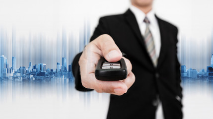 Businessman holding car remote, with modern buildings background, car safety