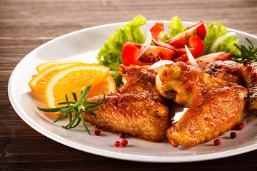 Roasted chicken wings with vegetable salad on wooden table