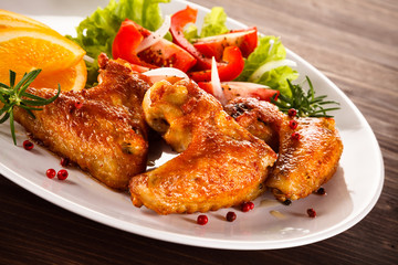 Roasted chicken wings with vegetable salad on wooden table