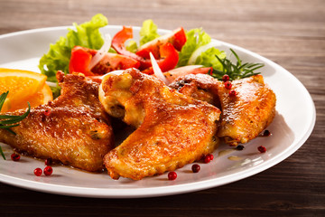 Roasted chicken wings with vegetable salad on wooden table