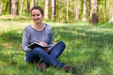 Naklejka na ściany i meble beautiful young girl in nature, making notes in a notebook