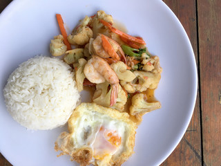 stir-fry vegetables with bean curd and shrimp in white dish with rice and fried egg on wooden background. Thai style Food.