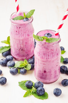 Violet blueberry fruit smoothie in glass jars with straw, mint leaves, berries. White wooden board background.