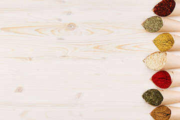 Decorative border of various powder spices close-up in paper corners on white wooden board with copy space.