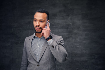 Stylish bearded black male in a grey suit talks on smart phone.