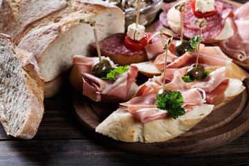 Spanish tapas with slices jamon serrano, salami, olives and cheese cubes on a wooden table