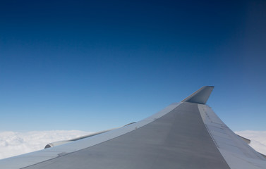 Fototapeta na wymiar Airplane Wing Flying Above Clouds. Plain Blue Sky Background