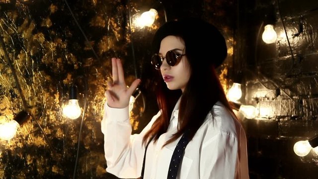 Young woman in sunglasses, beret and shirt on background wall with light bulbs