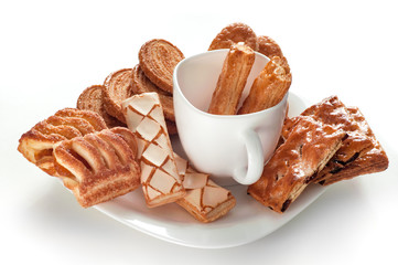 Many assorted cookies on a white saucer with a cup on white background