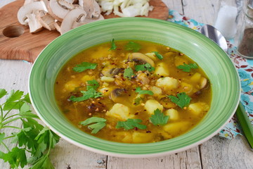 Healthy soup with buckwheat, potato, mushrooms, carrots and onion wit olive oi in a green bowl on a wooden background
