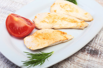 Slices of roasted chicken breast and tomato on white plate