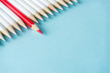 Business concept - lot of white pencils and color pencil on blue paper background. It's symbol of fight, leadership and communication.