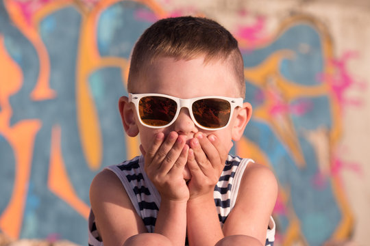 cute little boy wearing sunglasses closed his mouth with hands