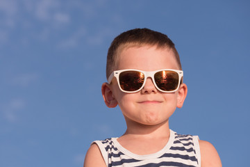 glad little boy wearing sunglasses on blue sky background