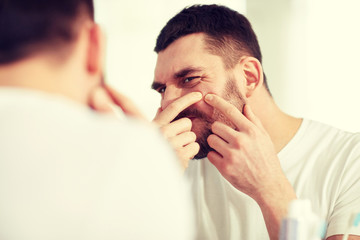 man squeezing pimple at bathroom mirror