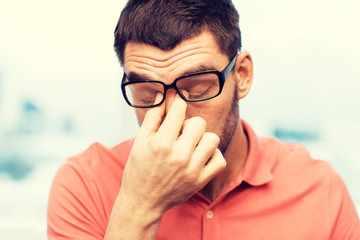 tired man in eyeglasses rubbing eyes at home