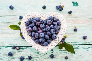 Tasty and fresh forest blueberries in a heart shaped bowl on wooden table.