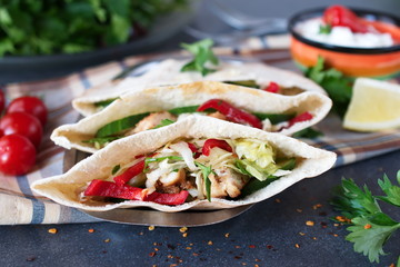 Pita filled with grilled chicken fillet, fresh salad, cucumber, sweet paprika, onion and yogurt sause on a grey abstract background. Home cooking. Easy and quick snack