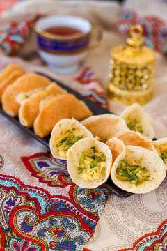 Traditional Arabic qataif pancake stuffed with cream and pistachios, prepared for iftar in Ramadan, oud in gold, on paisley background. Vertical