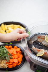 Young woman hands preparing fresh vegetable and fresh fish in steamer, healthy food