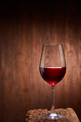 Red wine in the pure elegant wineglass standing on a wooden stand against wooden background.