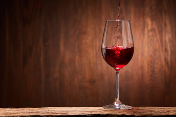 Tasty red wine poured in the elegant glass standing on the wooden stand against wooden wall background.