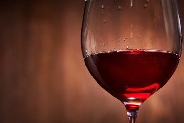 Elegant and fragile wineglass of tasty red wine against brown wooden background close-up.