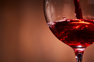 Close-up of brightly red wine poured in the wineglass and abstract splashing against brown background.