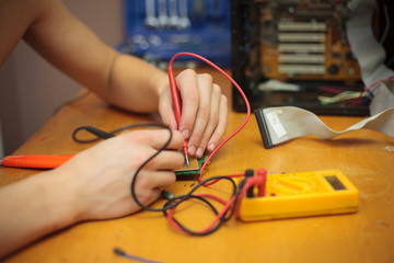 Young man hands measuring piece of a computer motherboard by electricity meter (color toned image)