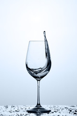 Pure water splashing in a wineglass while standing on the glass with water bubbles against light background.