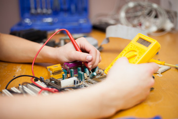 Young man hands metering a motherboard of PC by yellow electric meter